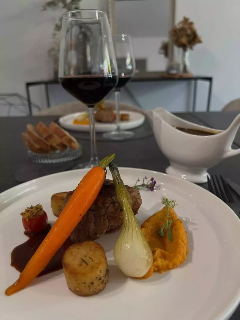 un repas à table en lien avec une prestation de chef privé et deux assiettes dressée esthétiquement avec un morceau de viande grillée et des légumes