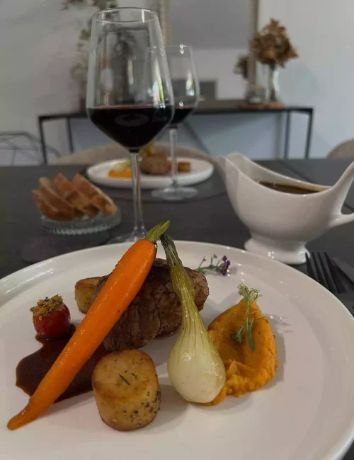 un repas à table en lien avec une prestation de chef privé et deux assiettes dressée esthétiquement avec un morceau de viande grillée et des légumes